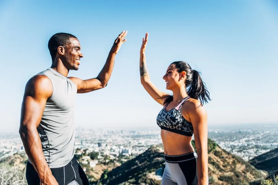 Two people high-fiving on a hilltop above a city
